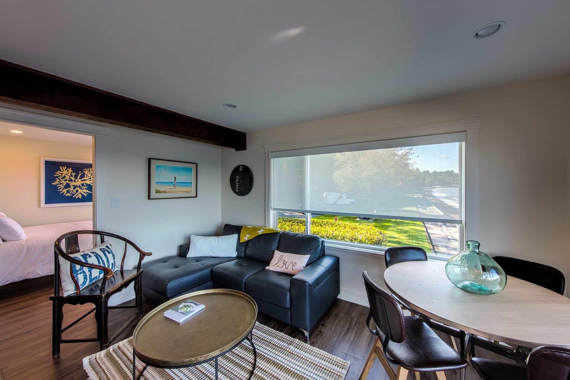 A modern living room with a sofa, a coffee table, and a dining table. There is a large window with a view of a green landscape.