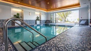 An indoor swimming pool with a wooden ceiling, tiled walls, and a view of the outdoors. - Qualicum Beach Ocean Suites  (Qualicum Beach)