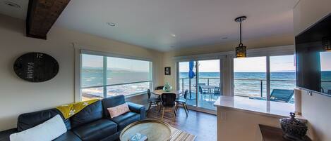 A living room with a large window overlooking the ocean, a sofa, a coffee table, and a dining area with a view.
