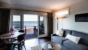 A living room with a sofa, a coffee table, and a dining table with chairs. There is a view of the ocean through a sliding glass door. - Qualicum Beach Ocean Suites  (Qualicum Beach)