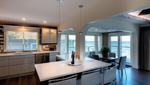 A modern kitchen with a central island, large windows, and a view of the sea. - Qualicum Beach Ocean Suites  (Qualicum Beach)