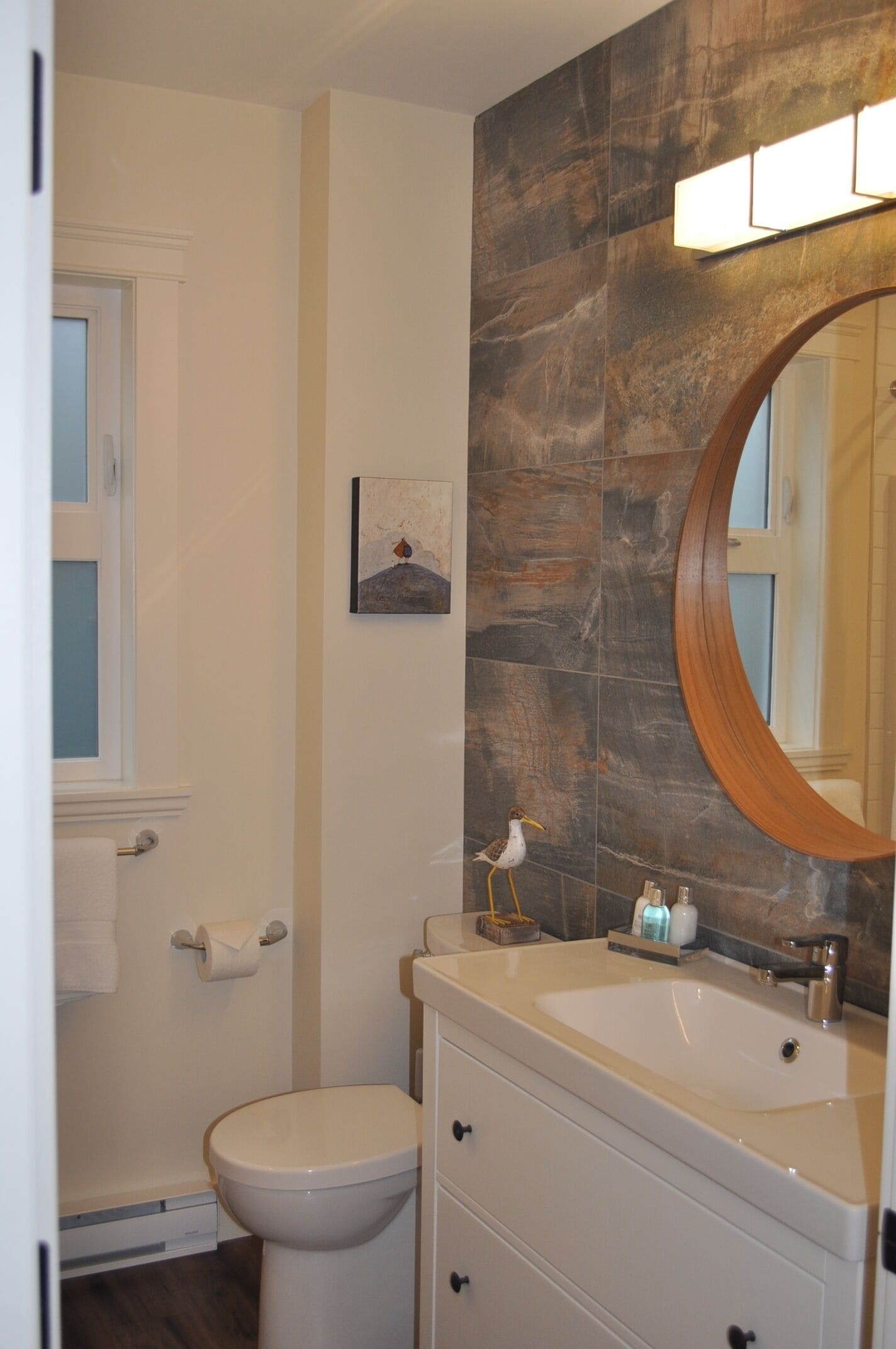 Un bagno con il water bianco, un lavabo con mobiletto in legno e uno specchio grande.