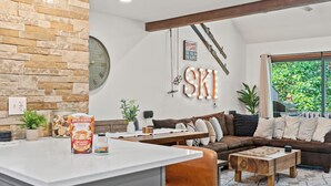 A cozy living room with a stone accent wall, a wooden ceiling beam, a large clock, and a sign that reads "Welcome, see you on the slopes." - Prime Location on Camelback Mtn, Renovated w/ Movie & Game Room | The Bear's Den (Tannersville)