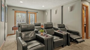 A room with six black leather reclining chairs, a small table with a plant, and a window with curtains.
