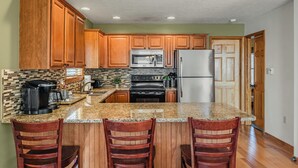 A kitchen with wooden cabinets, a granite countertop, a stainless steel refrigerator, and a black stove.