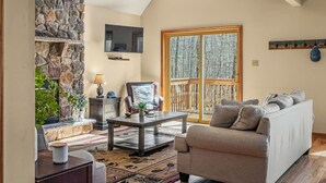 A living room with a stone fireplace, a sofa, a coffee table, and a TV mounted on the wall.