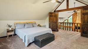 Un dormitorio con cama, mesita de noche, banco, ventilador de techo y puerta de madera.