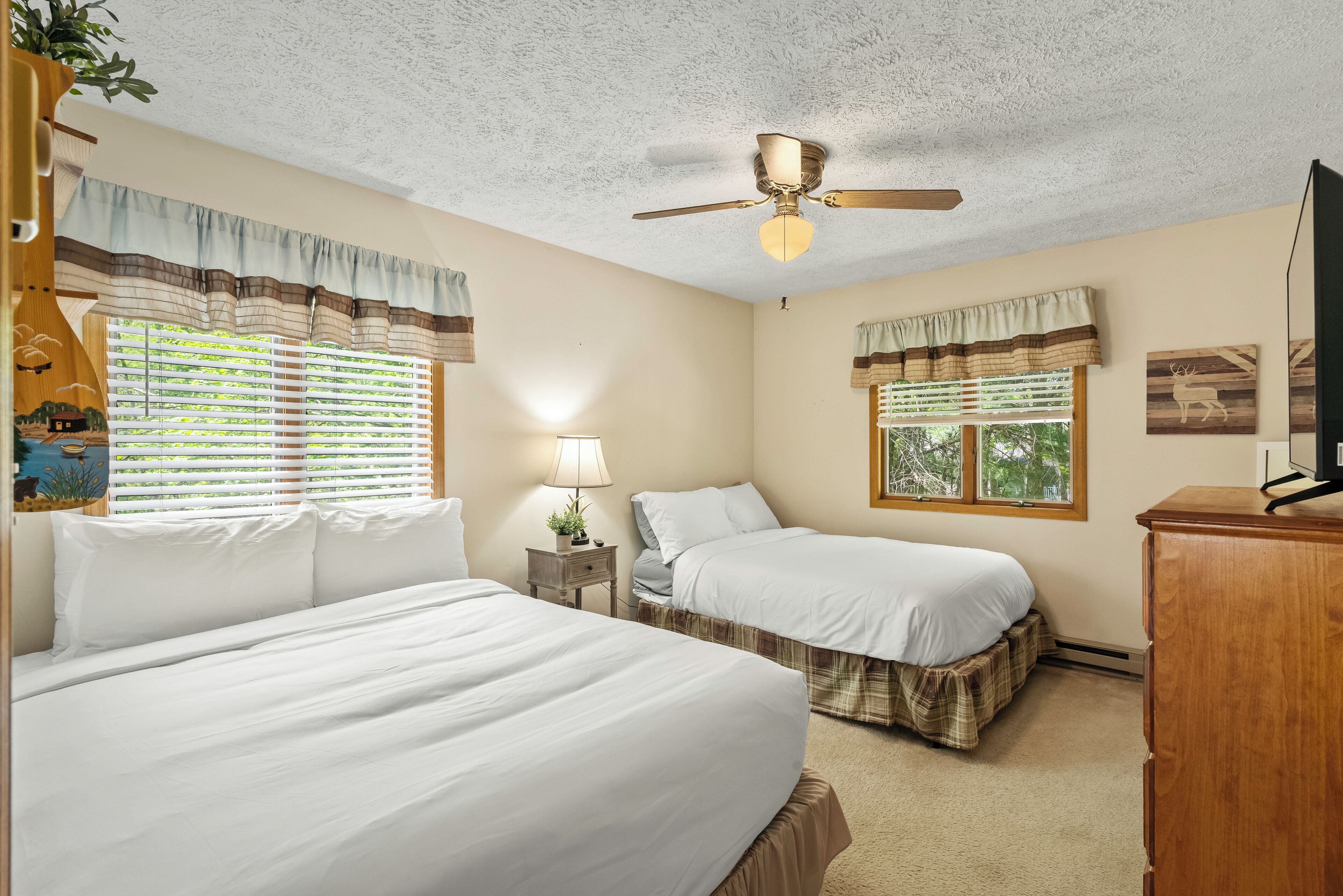 A room with two beds, a ceiling fan, a lamp, and a TV.
