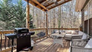 Eine überdachte Terrasse mit Grill, Gartenmöbeln und Blick auf einen Wald.