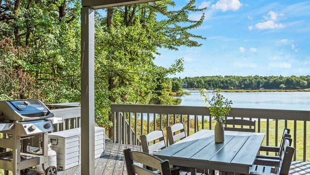 A wooden deck with a table and chairs, a grill, and a view of a lake. - Strawberry Shores by AvantStay | Lakefront Private Beach (Long Pond)