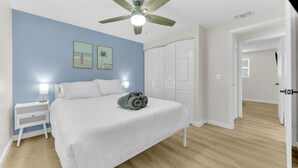 Ein Schlafzimmer mit einem Bett, Nachttischen, einem Deckenventilator und einer Tür zu einem anderen Raum.