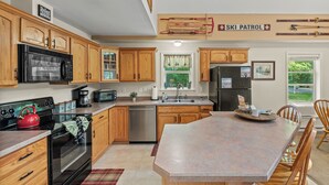Una cocina con armarios de madera, un refrigerador de acero inoxidable, un microondas y un hervidor rojo.