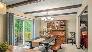 Een eetruimte met een houten tafel, bankjes en een kroonluchter. Er is een houten kast met glazen deuren en een bank met een kussen.