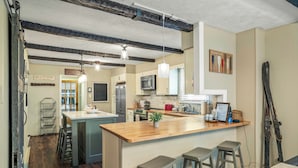 Een keuken met een houten kookeiland, barstoelen, een magnetron en een groot raam.