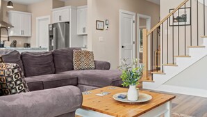 A modern living room with a gray sofa, a wooden coffee table, and a staircase. - Newly Built Lakefront w/ Deck & Views | Lakeside Serenity by AvantStay (White Haven)