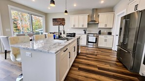 A modern kitchen with a large island, stainless steel appliances, and a view of autumn trees. - Newly Built Lakefront w/ Deck & Views | Lakeside Serenity by AvantStay (White Haven)
