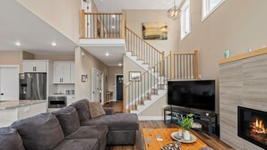 A modern living room with a grey sectional sofa, a wooden coffee table, a flat-screen TV, and a fireplace. - Newly Built Lakefront w/ Deck & Views | Lakeside Serenity by AvantStay (White Haven)