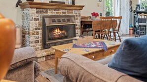 A cozy living room with a stone fireplace, wooden furniture, and a dining area. - Ridge Retreat by AvantStay | Game Room, Covered Porch, & Fire Pit! (Blakeslee)