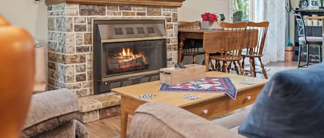 A cozy living room with a stone fireplace, wooden furniture, and a dining area.