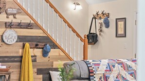 A staircase with wooden steps and a wall with various decorations including a clock, a welcome sign, and a wall-mounted bag. - Ridge Retreat by AvantStay | Game Room, Covered Porch, & Fire Pit! (Blakeslee)