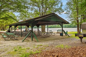 A covered picnic area with tables and benches, surrounded by trees and a body of water.
