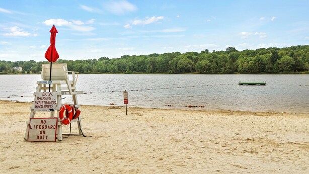 A lifeguard chair with red flags, a red umbrella, and signs indicating no lifeguard duty and required safety equipment. - Ridge Retreat by AvantStay | Game Room, Covered Porch, & Fire Pit! (Blakeslee)