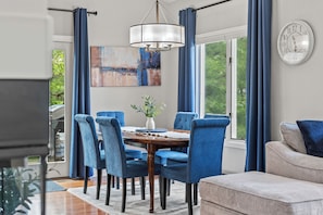 A dining area with a round table, blue upholstered chairs, a chandelier, and a painting on the wall.
