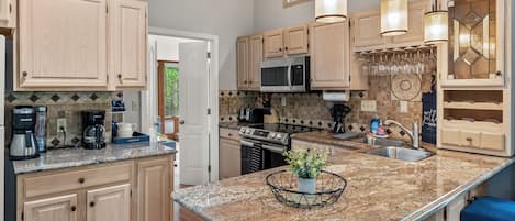 A modern kitchen with wooden cabinets, granite countertops, a built-in microwave, and a large island with bar stools.