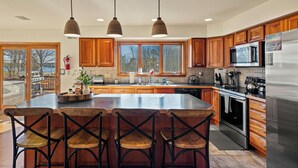 Una cocina con armarios de madera, una isla grande con taburetes de bar, electrodomésticos de acero inoxidable e iluminación colgante.
