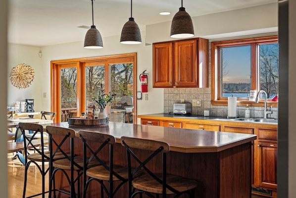 Una cocina amplia con armarios de madera, una isla grande con taburetes de bar y vistas al exterior a través de ventanas grandes.