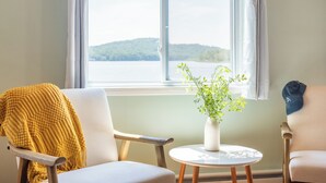 A room with two chairs, a small table with a plant, and a window with a view of a lake and hills. - The Lake Life by AvantStay | Lakefront + View + Hot Tub (Pocono Lake)