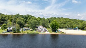 A lakeside property with a large house, a sandy beach, and a playground. - The Lake Life by AvantStay | Lakefront + View + Hot Tub (Pocono Lake)