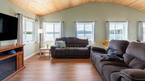A spacious living room with a high ceiling, wooden floors, a large flat-screen TV, and a sofa. - The Lake Life by AvantStay | Lakefront + View + Hot Tub (Pocono Lake)