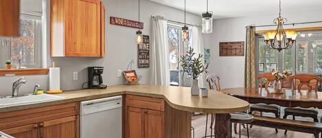 A modern kitchen with wooden cabinets, a dishwasher, and a dining area with a wooden table and chairs.