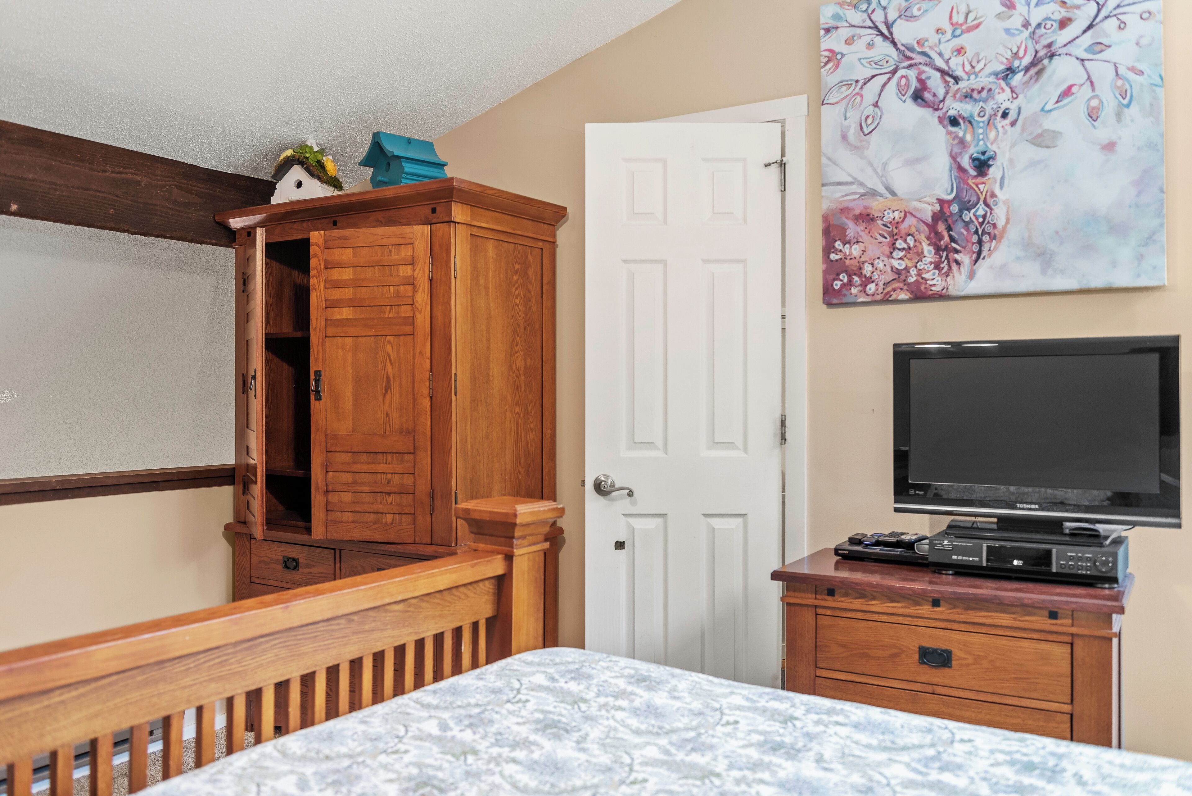 A bedroom with a wooden dresser, a television on a stand, and a painting of a deer on the wall.