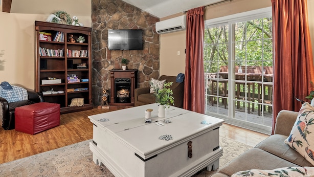 A living room with a stone accent wall, a fireplace, a large window with curtains, a bookshelf, and a flat-screen TV.