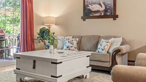 A living room with a white coffee table, a beige sofa with floral cushions, a painting of a swan, and a lamp.