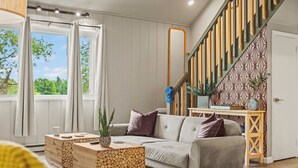 Ein Wohnzimmer mit grauem Sofa, einem Holztisch und einer Treppe mit einer Wand in geometrischem Muster.