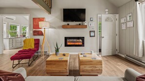 Ein modernes Wohnzimmer mit Kamin, Flachbildfernseher und Essbereich mit Holztischen.