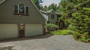 Une maison à deux étages avec un garage, une véranda et une allée gravillonnée.