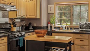 Une cuisine avec des meubles en bois, une cuisinière, un évier et une fenêtre donnant sur les arbres.