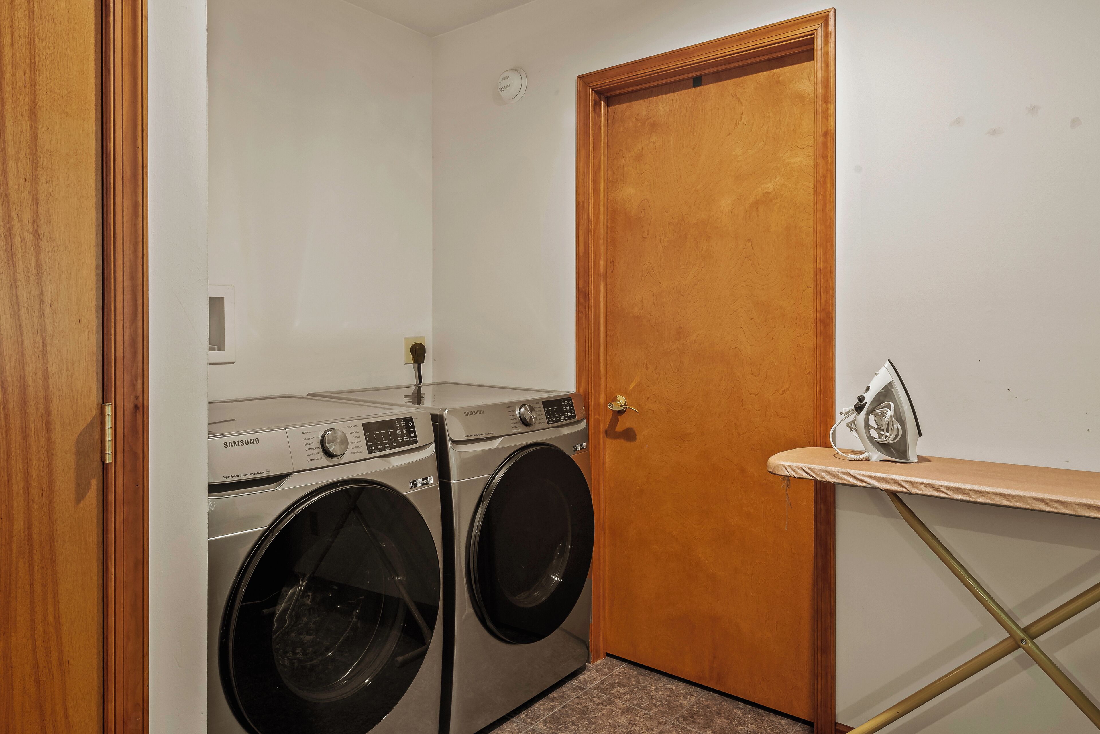 A laundry room with two Samsung front-loading washers and a wooden door.