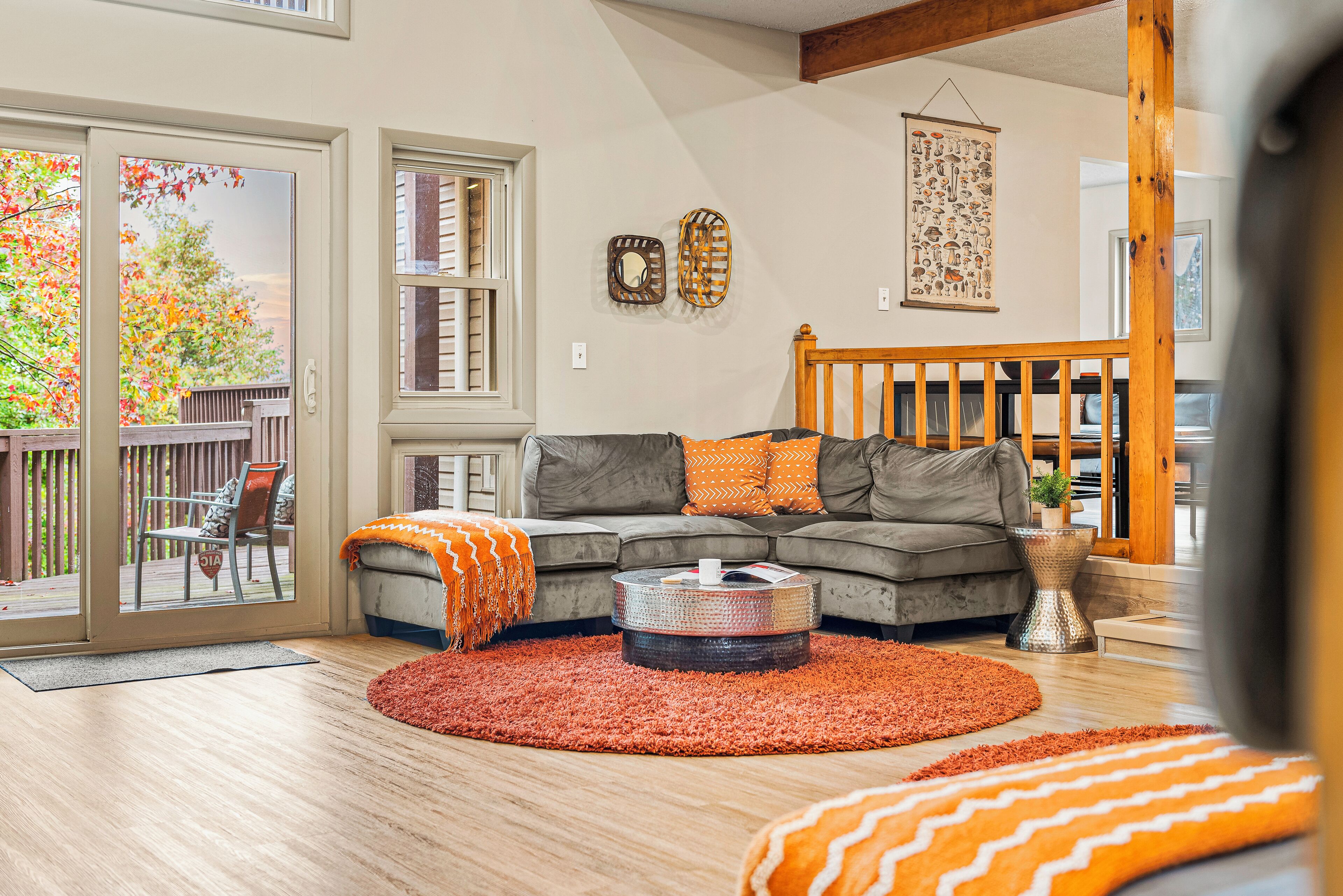Un salon avec un canapé gris, des coussins de couleur orange, une table basse ronde et un tapis rouge.