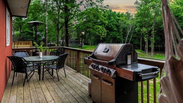 A wooden deck with a grill, a table with chairs, and a potted plant.