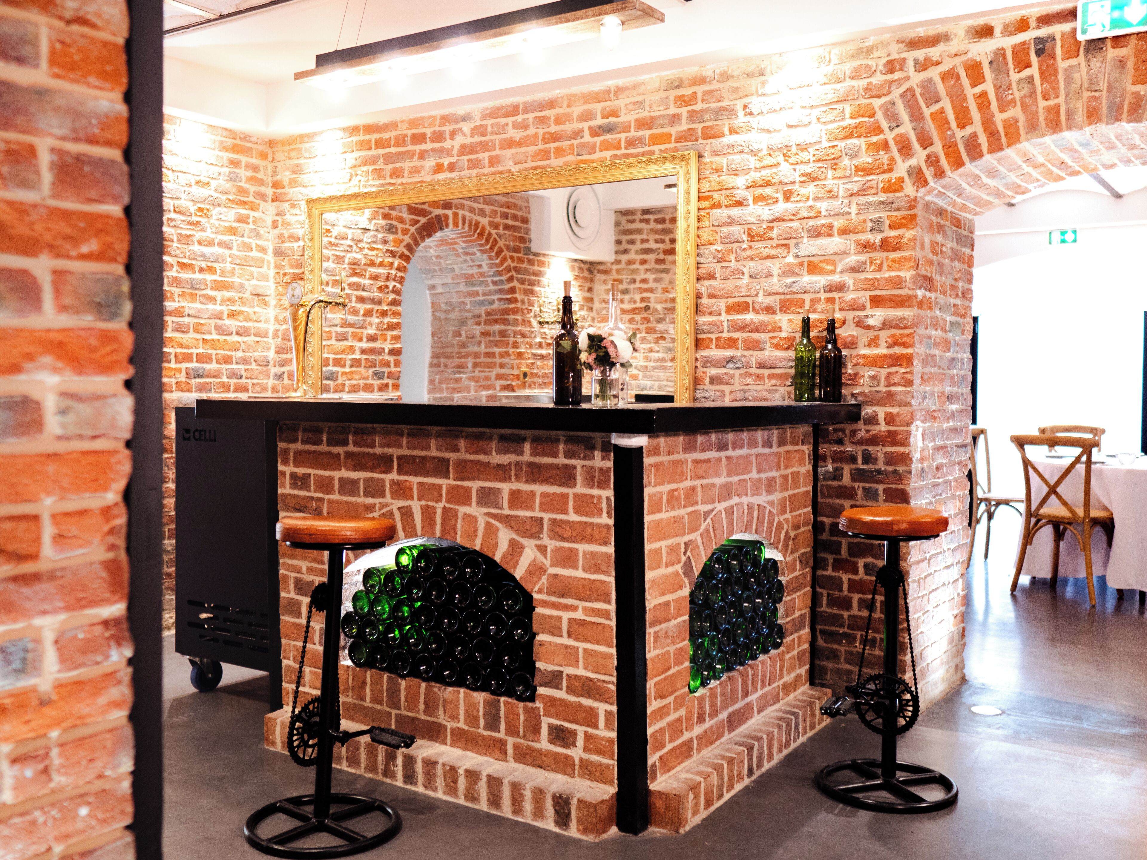 Una zona de bar con pared de ladrillo, espejo y taburetes.