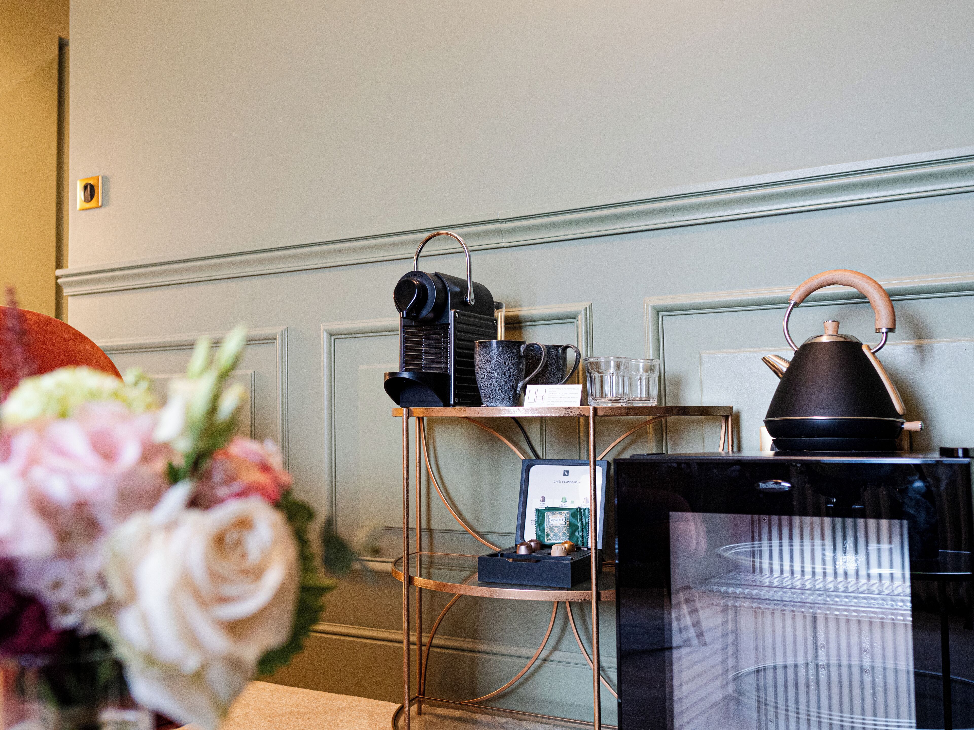 A room with a coffee station featuring a kettle, cups, and a coffee machine.