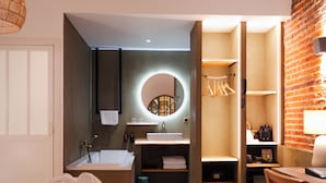 A modern bathroom with a bathtub, sink, and mirror. There is a towel rack and a small shelf with toiletries. - Hotel Château Héloïse (Mérélessart)