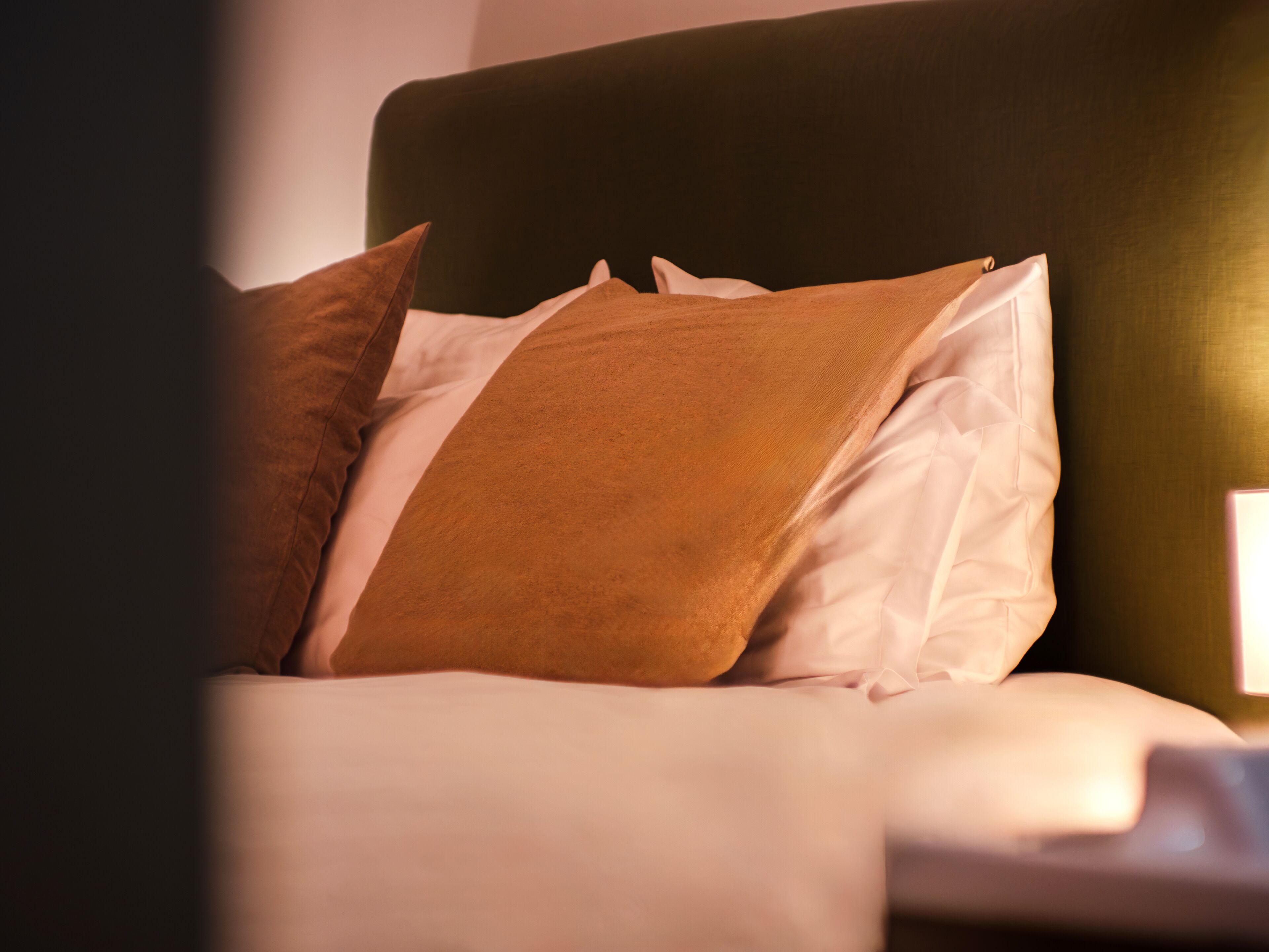 Cama com cabeceira escura e várias almofadas.