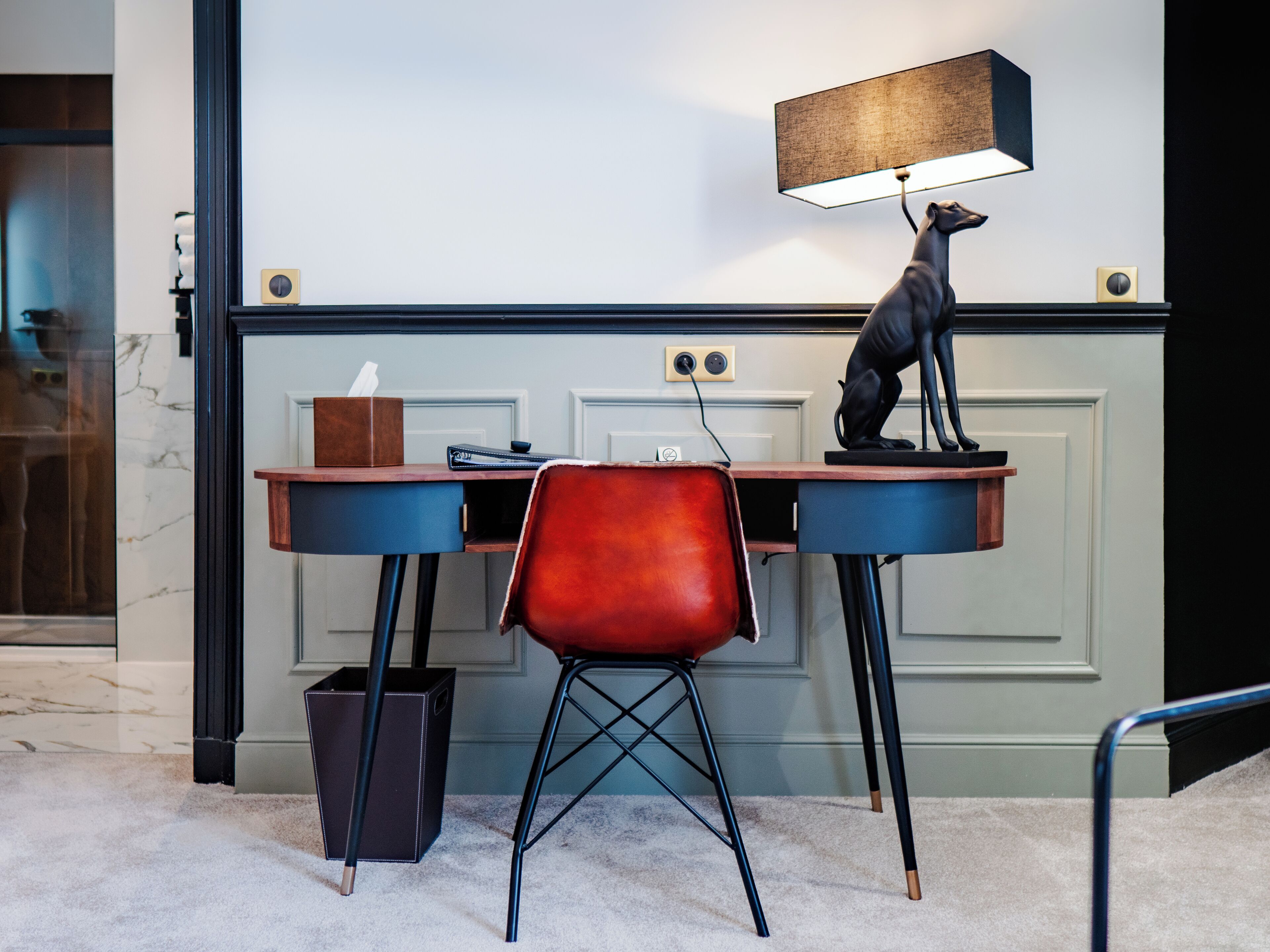 Een bureau met een lamp, een stoel en een beeldje.