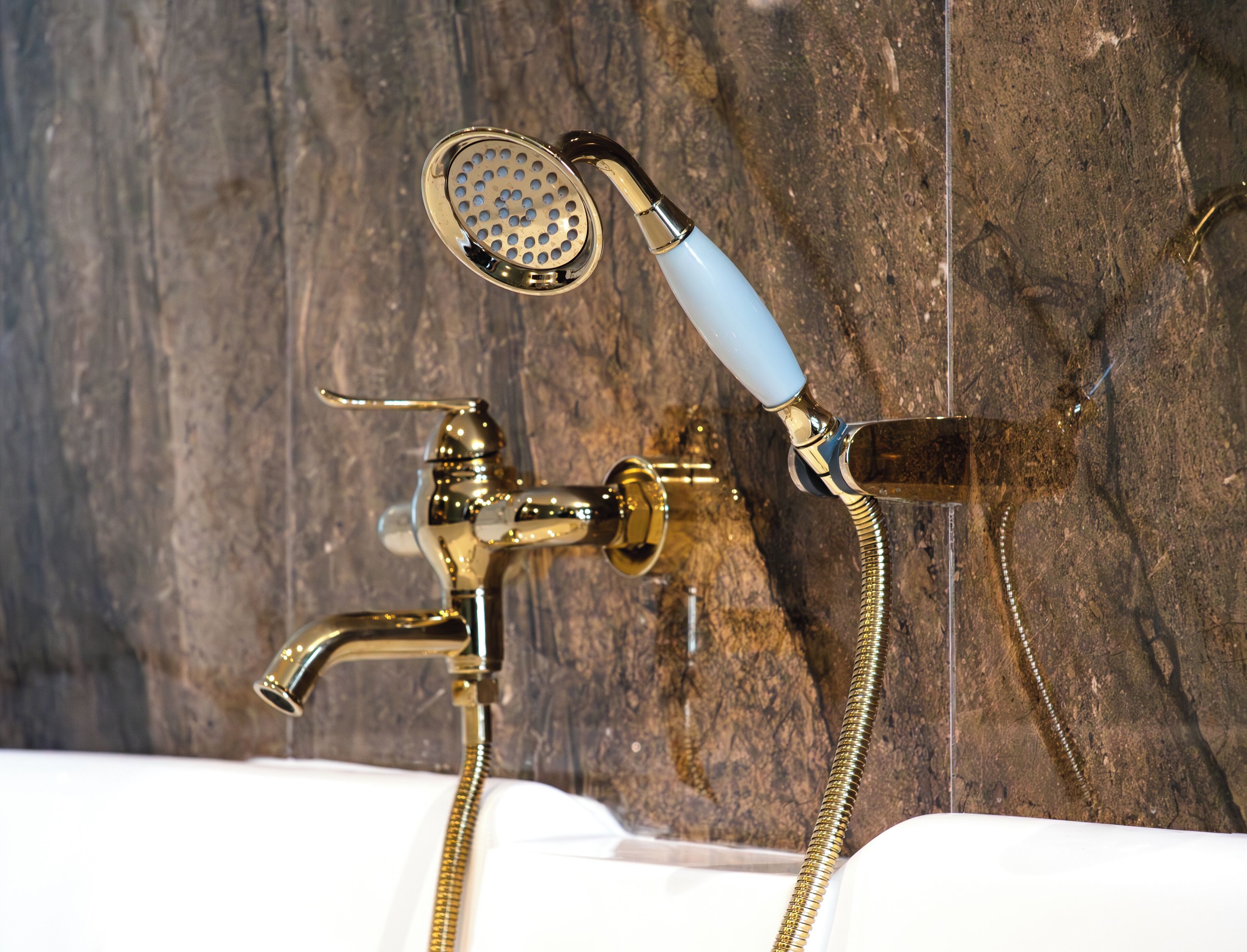 Un baño con ducha y grifo de latón, un lavabo blanco y una pared de madera.